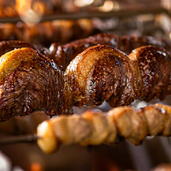 Skewers of picanha and other meats cooking over an open flame at a Brazilian steakhouse.