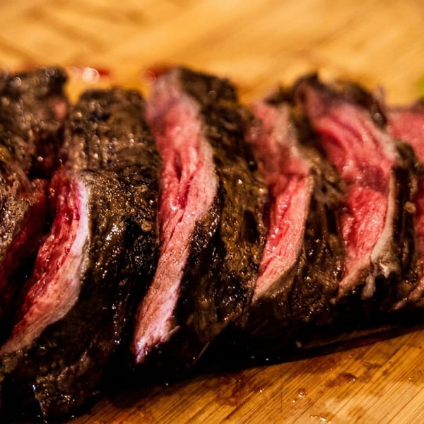 Sliced medium-rare steak with a dark crust on a wooden cutting board, garnished with greens.
