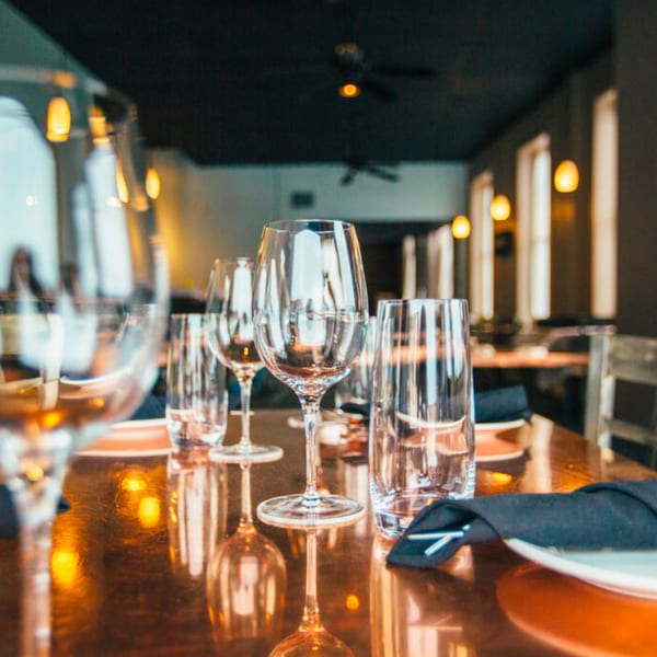 Set table with wine glasses, water glasses, and plates with black napkins in a restaurant.