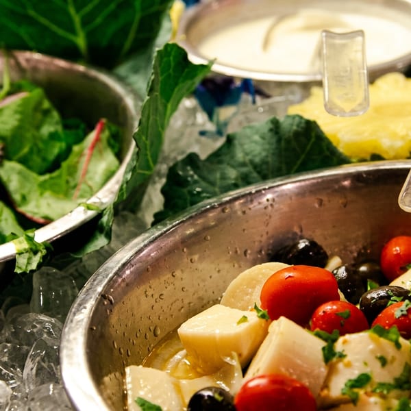 A salad bar with bowls of fresh greens, cherry tomatoes, olives, and hearts of palm on ice.